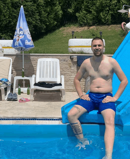 a shirtless man in blue shorts sits on a blue float in a pool