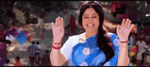 a woman in a blue and white saree is smiling and waving her hands in the air .