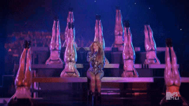 a woman is singing into a microphone on a stage surrounded by a group of dancers .