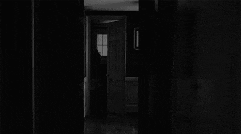 a woman in a white dress is standing in a dark hallway .