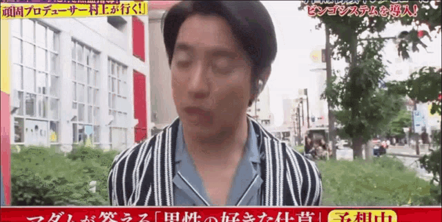 a man in a striped shirt is standing in front of a building with chinese writing on it