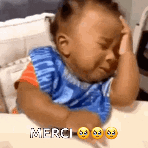 a baby in a blue shirt is crying and the words merci are below him