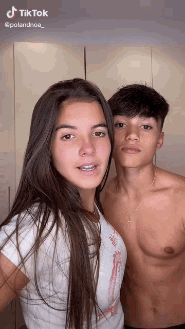 a man and a woman are posing for a picture together . the woman is wearing a white shirt and the man is shirtless .