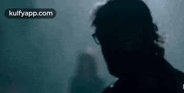 a man with glasses is standing in a dark room .