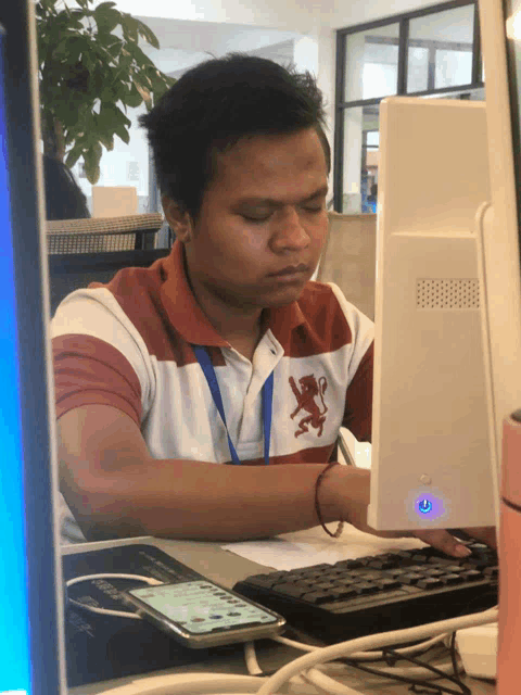 a man wearing a red white and blue polo shirt with a lion on it sits in front of a computer