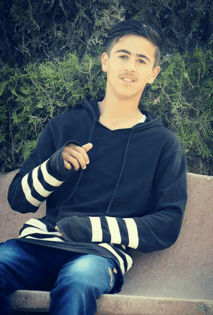 a young man wearing a black and white striped sweater is sitting on a bench