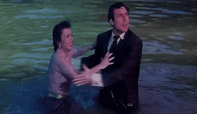 a man in a suit holds a woman in a dress in the water