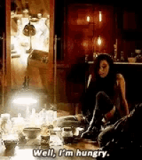 a woman is sitting on the floor in front of a table and saying well , i 'm hungry .