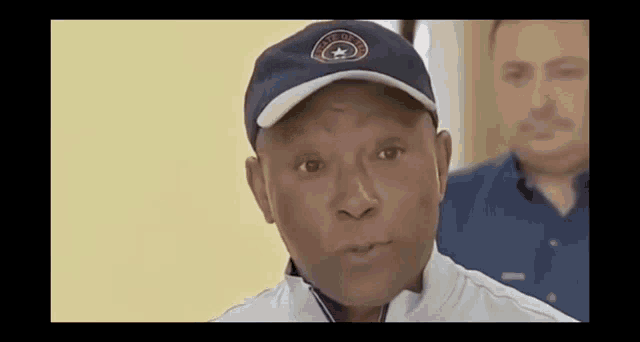 a man wearing a baseball cap and a white jacket is talking to another man .
