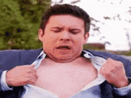 a man is sitting on a couch taking off his shirt and making a funny face .