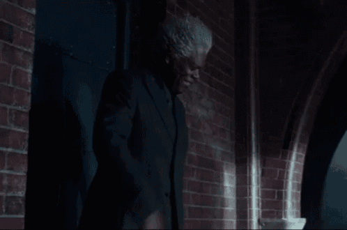 a man in a black suit is standing in front of a brick wall