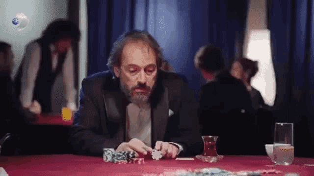 a man in a tuxedo is sitting at a table playing poker and drinking tea .