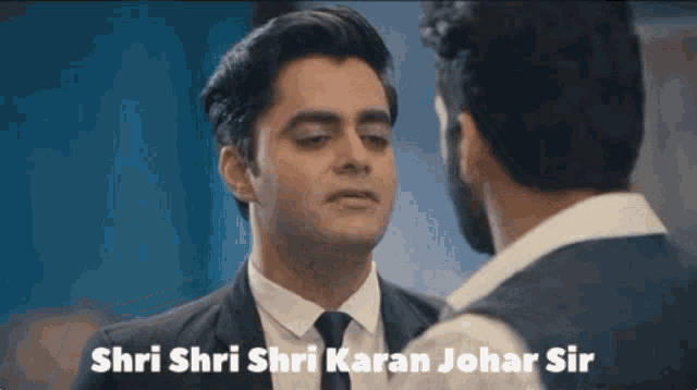 a man in a suit and tie is talking to another man with the words shri shri shri karan johar sir written below him