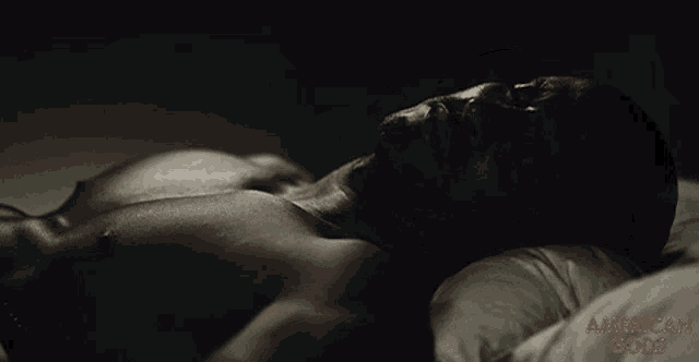 a shirtless man is laying on a bed with the words american gods on the bottom right
