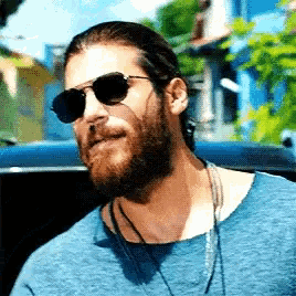 a man with a beard and sunglasses is wearing a blue shirt and necklace .