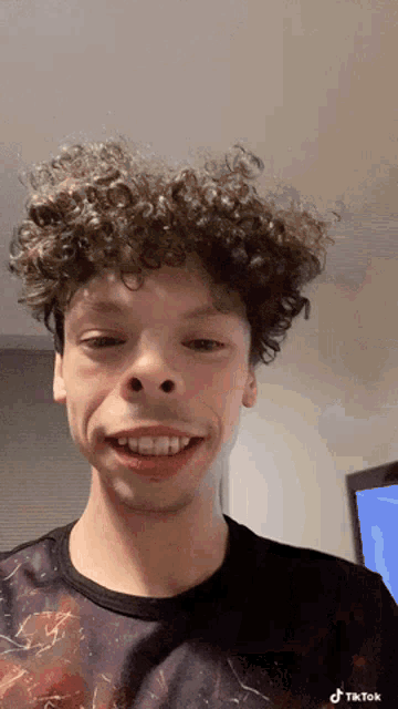 a young man with curly hair is smiling with a tiktok watermark on the bottom right