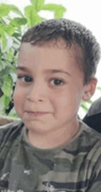 a close up of a young boy wearing a camouflage shirt .