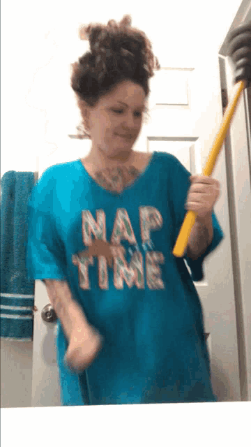 a woman in a blue shirt that says nap time is holding a yellow mop