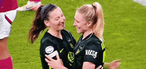 two women are hugging each other on a soccer field and smiling .