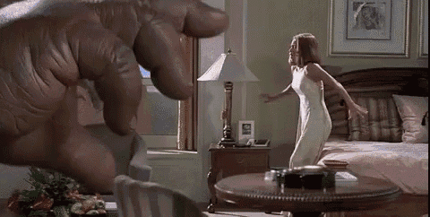 a woman in a white dress is dancing in a living room with a giant hand behind her .