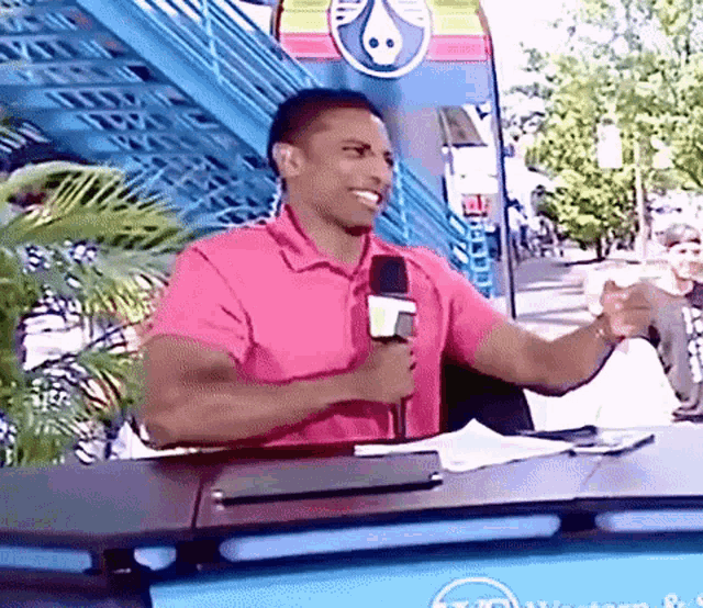 a man in a pink shirt is holding a microphone and talking