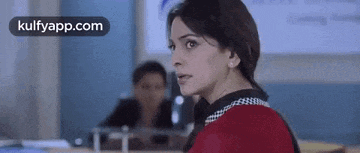 a woman is sitting in a classroom with a man in the background and looking at the camera .