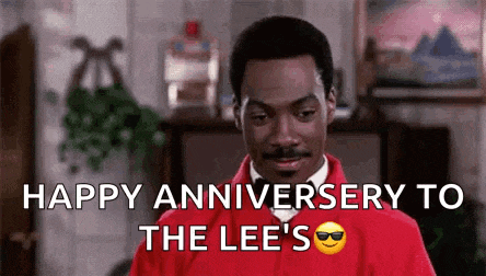 a man in a red jacket and tie is saying `` happy anniversary to the lee 's '' in a living room .