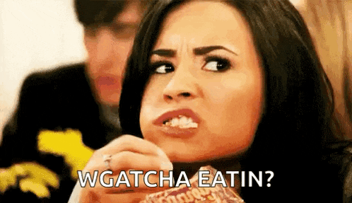 a woman is eating a hamburger and making a funny face while a man looks on .