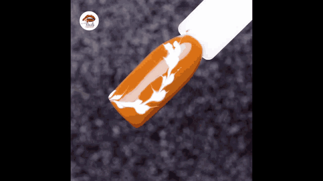 a close up of an orange nail with a white leaf design on it