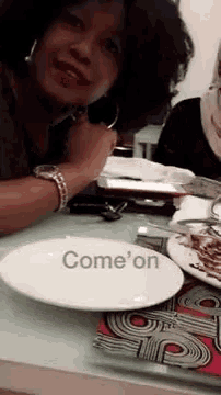 a woman is sitting at a table with a plate that says come on on it