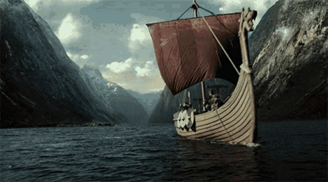 a boat with a red sail is floating on a lake with mountains in the background