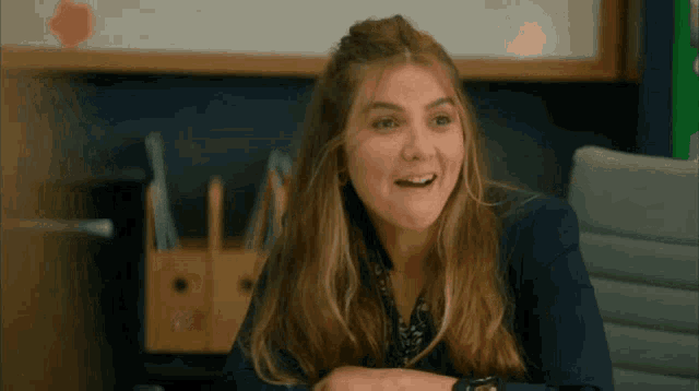 a woman is smiling while sitting at a desk in front of a white board .