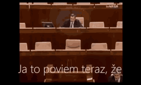 a man in a suit sits at a desk with a laptop in front of him and the words ja to poviem teraz