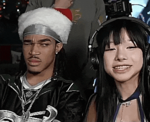 a man and a woman are wearing headphones and making funny faces . the man is wearing a santa hat .