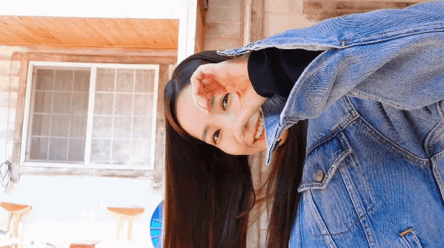 a woman wearing a denim jacket is smiling and covering her face with her hand