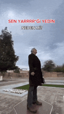 a man in a black coat stands in front of a sign that says sen yarrr * gi yedin neden mi ?
