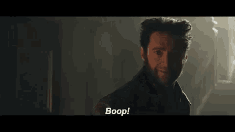 a man in a dark room is pointing at the camera and says boop .