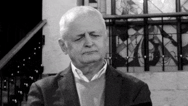 a man in a suit and sweater stands in front of a stained glass window