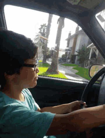 a young boy wearing glasses is driving a car and looking out the window