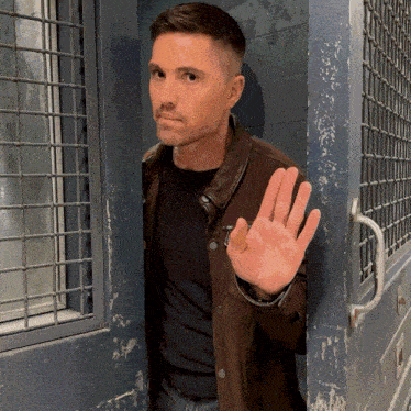 a man in a brown jacket is standing in a doorway with his hand out