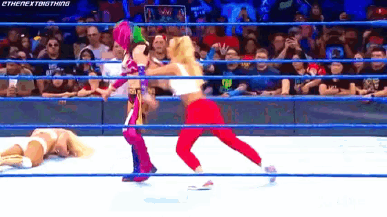 two women are wrestling in a wrestling ring while a crowd watches .