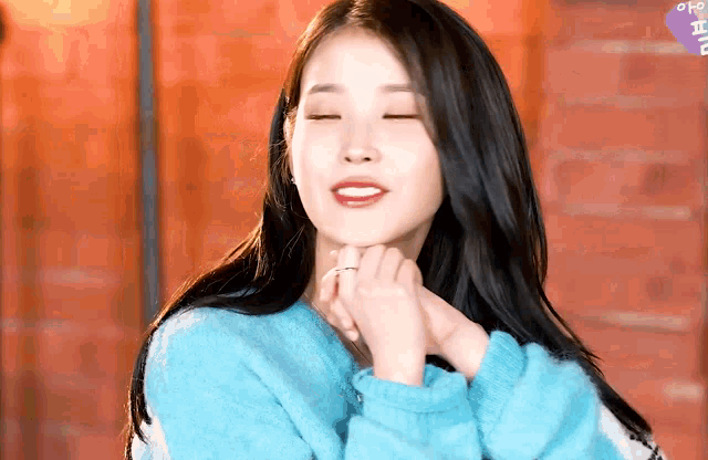 a woman in a blue sweater has her eyes closed and her hands on her face