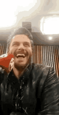 a man in a leather jacket is laughing while holding a stuffed animal in his hand .