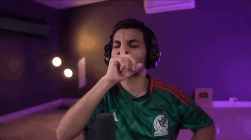 a man wearing headphones and a green shirt is covering his mouth .