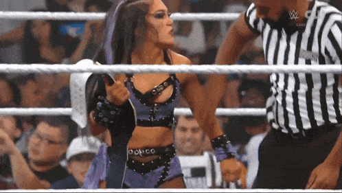 a woman in a purple outfit is standing in a wrestling ring with a referee in a black and white striped shirt