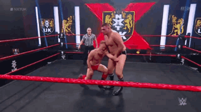 two men are fighting in a wrestling ring with a referee watching .
