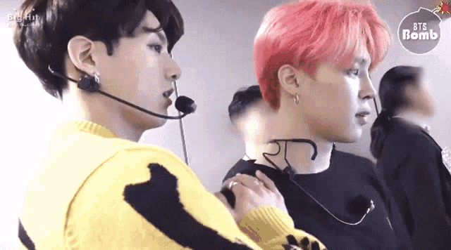 a man with pink hair is talking into a microphone while another man looks on