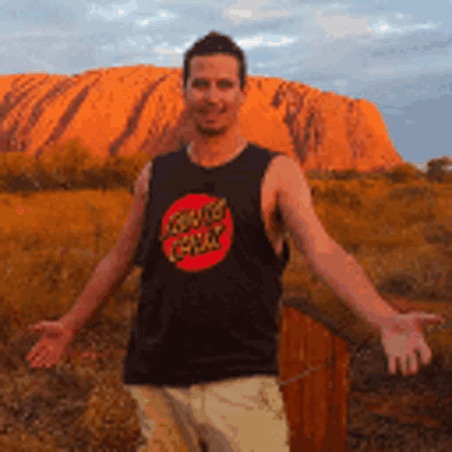 a man wearing a black santa cruz tank top stands in front of a mountain