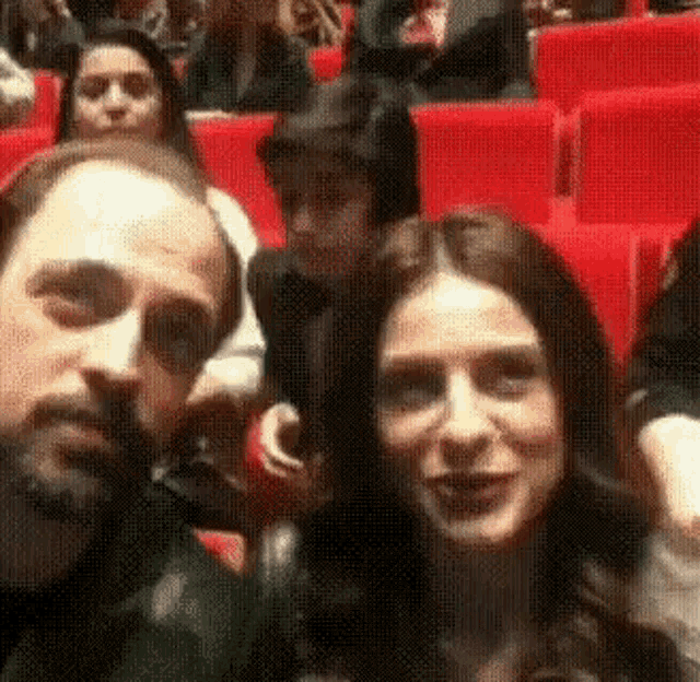 a man and a woman are taking a selfie in a theater while sitting in red seats .