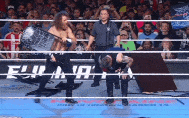 two men are wrestling in a ring with a crowd behind them and a sign that says ' wwe ' on it